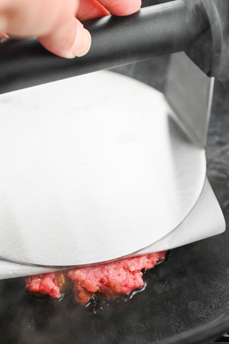 Smashing a burger patty with burger press. 